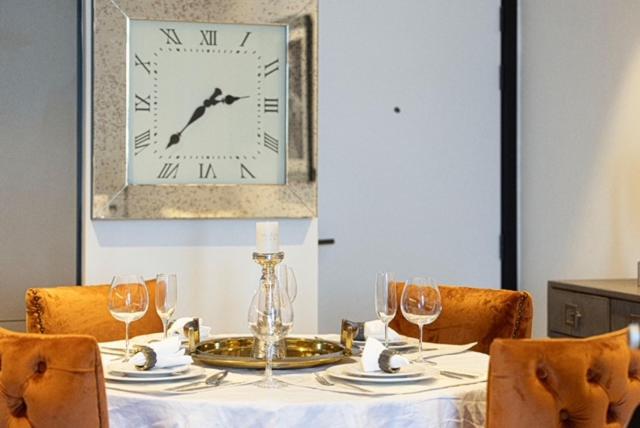 Dining table set with glassware and velvet chairs beneath a wall clock